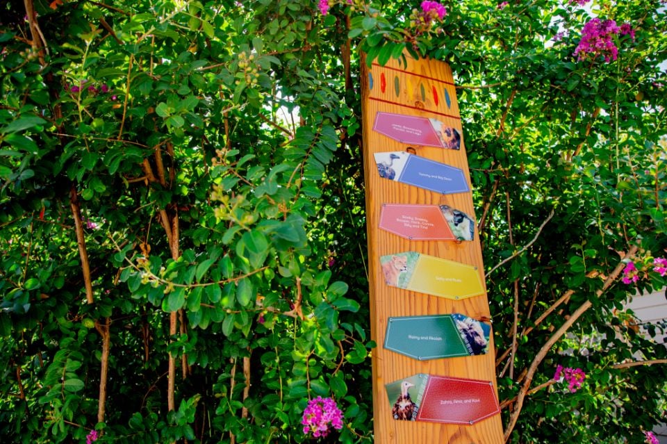 A wooden Tulsa Zoo signpost covered with colorful animal plaques, surrounded by greenery